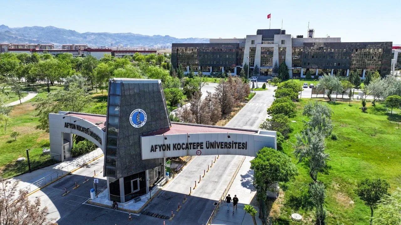 Pintu gerbang Afyon Kocatepe Üniversitesi dengan papan nama kampus, gedung modern, dan pepohonan hijau dari udara